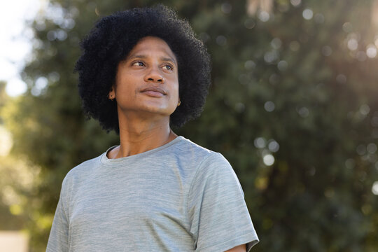 Adult African American man standing outdoors in park wearing light gray t-shirt and hoop earring
