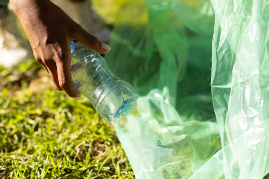 Woman's hand holding clear plastic water bottle and placing it into green collection bag on grass