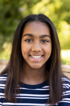 African American female teen smiling while sitting outdoors on bench wearing navy blue striped top