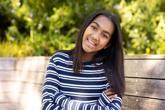 African American youth smiling, sitting on wooden bench in garden in navy striped top, studs