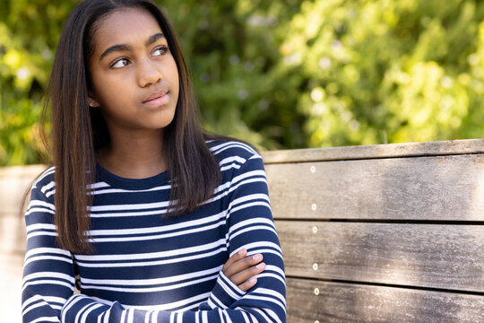 Teen African American girl sitting on park bench, wearing striped top and stud earrings