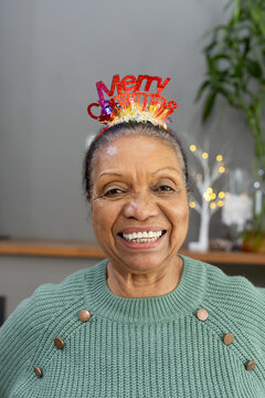 Senior woman smiling, wearing Christmas headband, green sweater, looking at camera at home