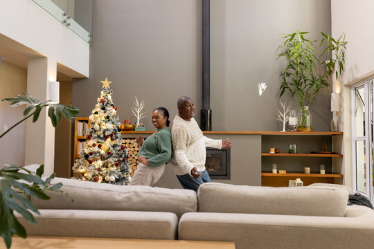 African American couple standing back-to-back in living room with lit Christmas tree, fireplace