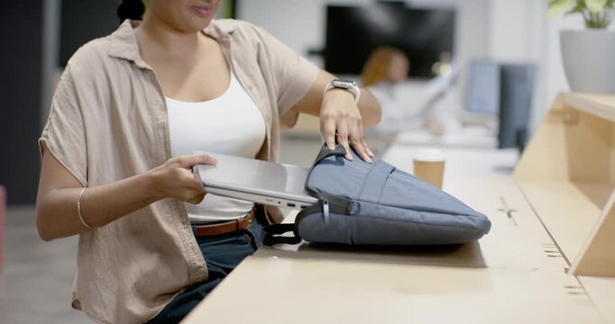 After work Indian woman packing laptop into blue sleeve at coworking counter, grabbing coffee