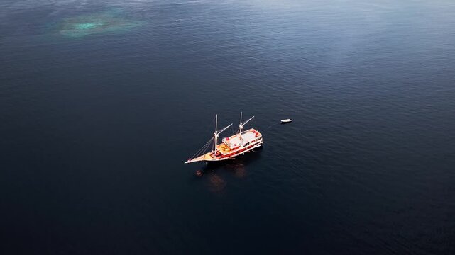 Tomia, Indonesia - 09 August 2026: Aerial view of a traditional phinisi boat sailing on the calm blue waters of Wakatobi Regency.