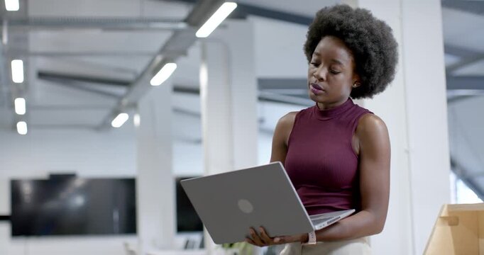Spotting detail on laptop, African woman in maroon top by office column typing to review report