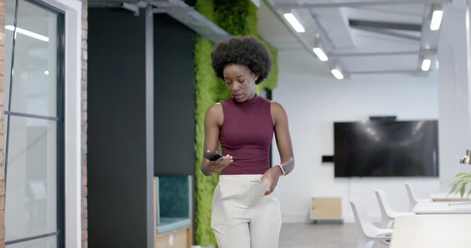 Woman walking in open office glancing at phone, scrolling text then answering call in maroon top