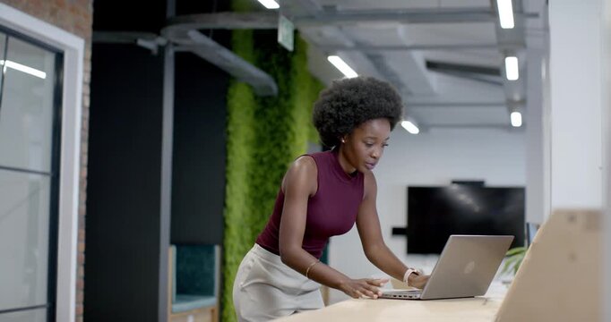 African American woman maroon top finishing task typing closing laptop at counter in office packing