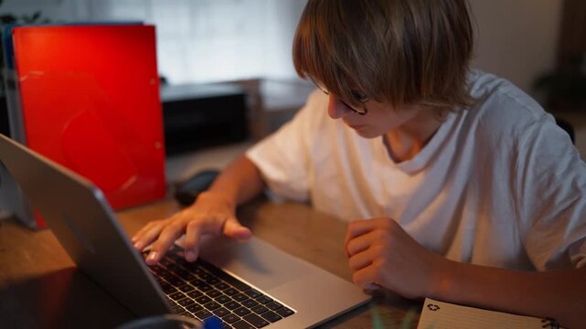 Young student focused on schoolwork at home using a laptop and notebook. Academic success, education, learning, concentration, productivity and future achievement concept.