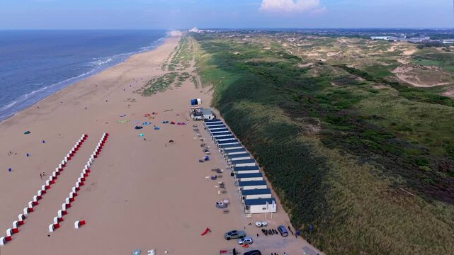 Aerial view video clip of Katwijk aan Zee beach resort, red and white beach cabins, beach houses, coastal sand dunes, Scheveningen skyline, and North Sea waves in South Holland, Netherlands