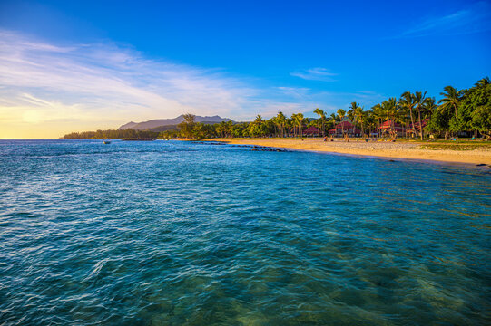 Sunset light over Bel Ombre beach in southern Mauritius, with turquoise Indian Ocean water, palm-lined shore, distant mountains, and a calm tropical mood.