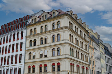 Obraz premium Low angle view of a beautiful historic European building with an ornate beige facade, arched windows, and red awnings under a cloudy sky.
