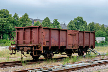 Fototapeta premium An abandoned weathered red brown steel cargo wagon standing on a railway siding track surrounded by grass.