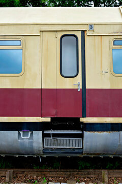 Side view of an old classic beige and red passenger train car showing the entrance door with steps and window.