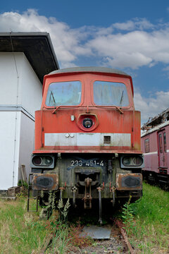 A frontal shot of a powerful vintage red train engine sitting on rails with green grass growing around.
