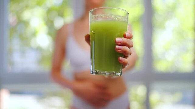 Woman is holding a glass of selery juice in her hand and shows a thumb up.
