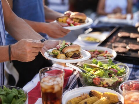 Labor Day Barbecue mit Cheeseburger, gegrilltem Mais und frischem Salat: G&auml;ste bedienen sich bei einem sommerlichen amerikanischen Grillbuffet im Freien.