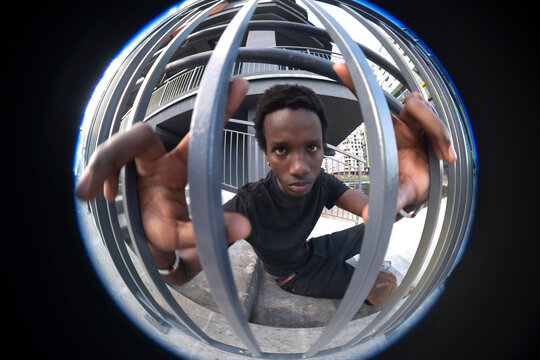 Determined young black man looking through metal fence in city with copy space