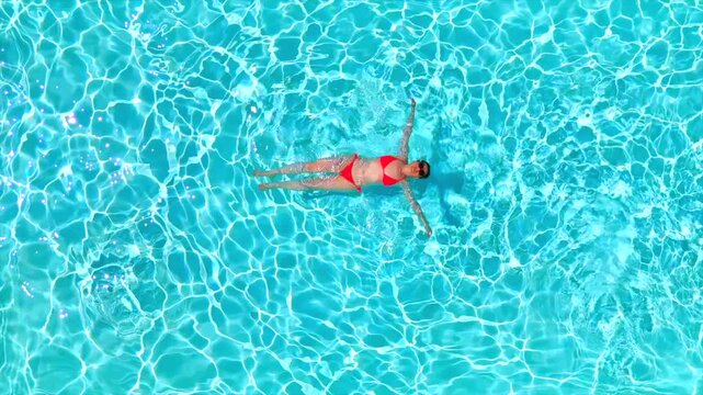 Top down view of a woman in pink swimsuit laying on her back in the pool.