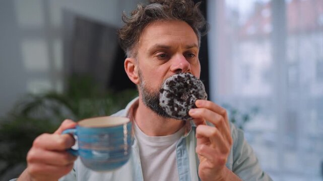 Sweet addiction concept. A man eats a donut and drinks coffee. 