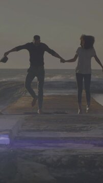 Animation of spot of light against african american couple walking on the rocks near the sea