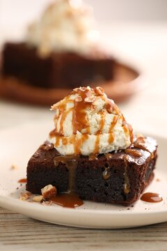 Delicious brownie with vanilla ice cream, caramel sauce and nuts on wooden table, closeup