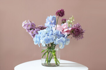 Obraz premium Bouquet of beautiful flowers in vase on white table near beige wall indoors, closeup