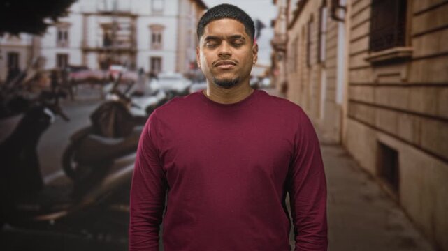 Hispanic man with beard standing facing camera, eyes closed then smiling across frames, wearing maroon shirt on a street; serenity presence.