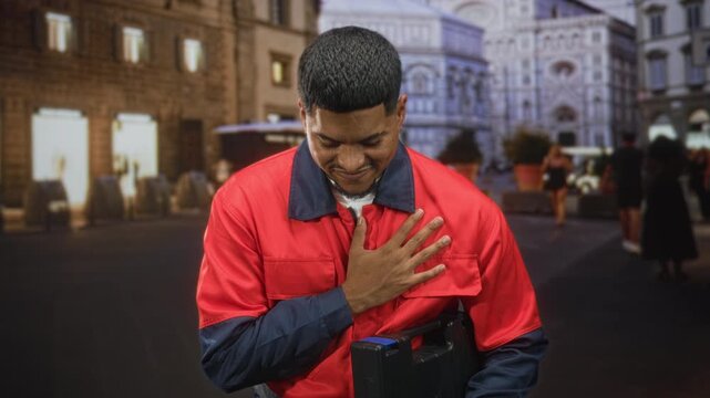 Man repairman in red uniform holding toolbox places hand on chest on street by a historic cathedral facade; gratitude duty.