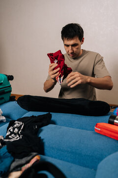 Vertical portrait of traveler male meticulously folding clothes and packing them into a suitcase, preparing for a journey and organizing personal belongings for an upcoming trip or holiday.