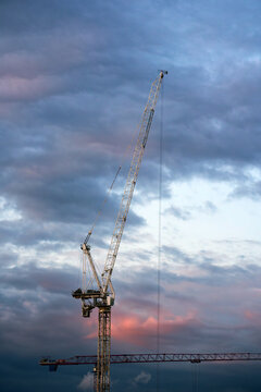 Construction crane towering against a dramatic cloudy sunset sky. Industrial machinery for building infrastructure and urban development. Equipment for engineering project and skyline