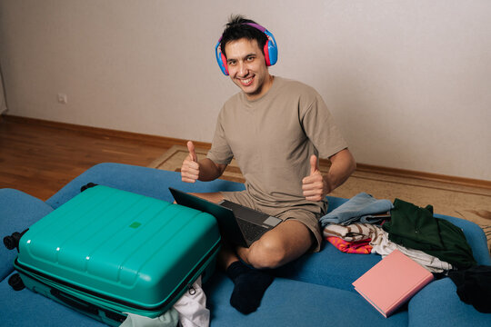 Cheerful male traveler packing suitcase and checking laptop, embracing remote work freedom and wanderlust as he prepares for joyful travel adventure and new destinations, smiling looking camera.