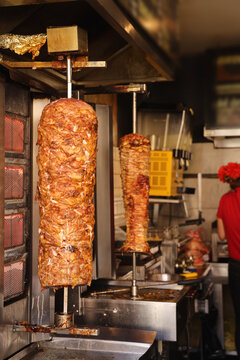 Traditional street food doner kebab or shawarma on vertical rotisserie. Rotating shawarma meat grilling on spit inside street food shop. Concept of street food, fast food culture, authentic cuisine