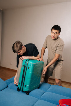Vertical portrait of two traveler male preparing for travel, holding a vibrant turquoise luggage case, focusing on protection and security with plastic wrap for his upcoming vacation.