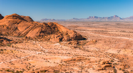 Obraz premium An aerial perspective shows the vast desert landscape of Spitzkoppe in Namibia, featuring large granite rock formations, dry plains, and distant mountains.