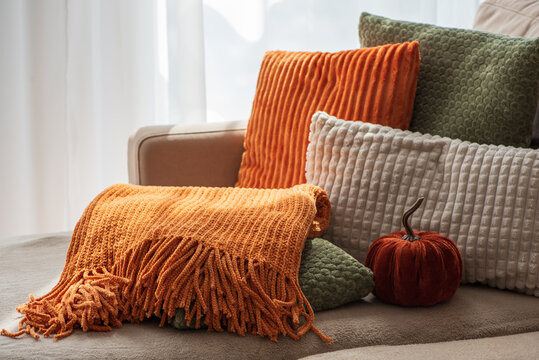 Cozy autumn throw blanket and decorative pillows arranged on a comfortable sofa with a small pumpkin accent