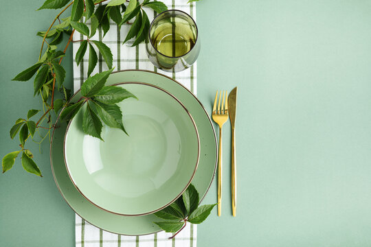 Elegant Table Setting for Autumn Harvest Celebration with Green Plates and Gold Cutlery Amidst Vibrant Foliage