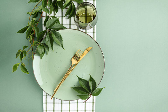 Elegant Table Setting with Golden Cutlery Green Plate and Fresh Leafy Vine Accents