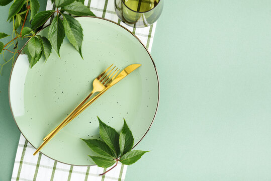 Elegant table setting with pastel plate golden cutlery green leaves and checkered napkin for seasonal celebration