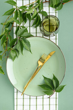 Elegant pastel green plate set with golden cutlery and fresh green leaves on checkered cloth for festive dining