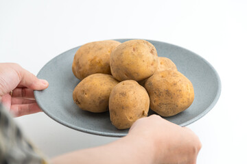 Fototapeta premium Hands holding and arranging fresh raw baby potatoes on grey ceramic plate isolated on white