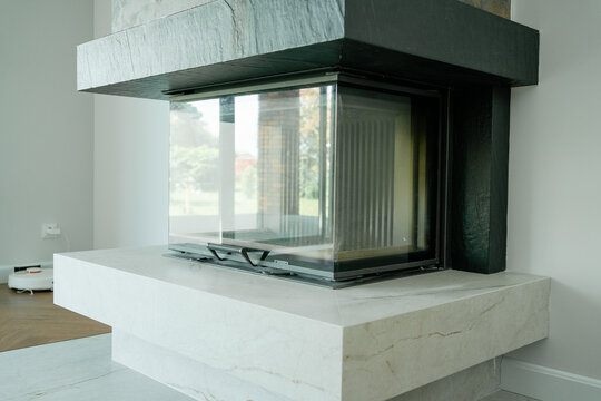 Modern fireplace with panoramic glass door and stone hearth in a spacious contemporary living room. Ideal stock image for interior design, fireplace heating, home comfort, and luxury living