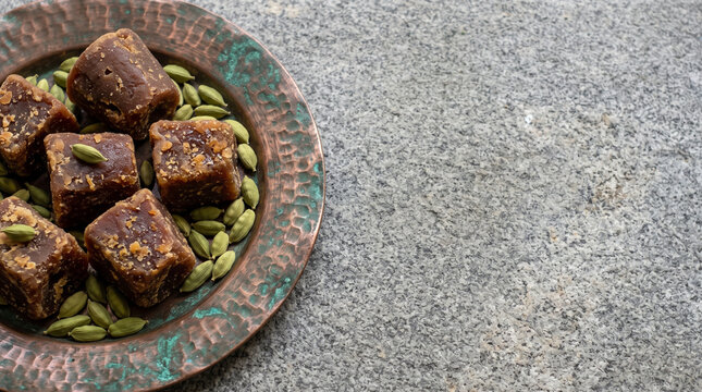 Raw dark jaggery and cardamom on copper plate