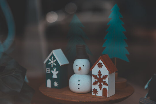 Charming wooden Christmas display featuring a cute snowman figurine, Decorated tiny houses and minimal evergreen trees, Rustic holiday village concept with cozy winter atmosphere for seasonal design.