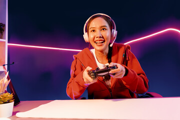 Host channel of smiling beautiful Asian girl streamer with joystick playing online game wearing headphones paste talking with viewers media online. Esport skilled team players in neon room. Stratagem. © InfiniteFlow