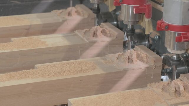Close-up of a multi-spindle CNC router machine milling intricate carved decorative patterns into wooden workpieces in a furniture manufacturing workshop.
