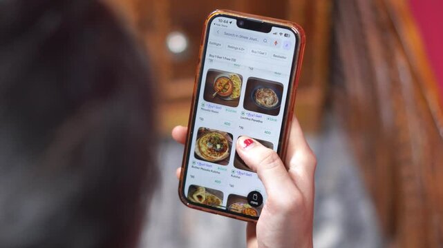 Indian Woman Selecting Dishes on Smartphone Menu Screen for Online Meal Ordering. Browsing Online Food Ordering Marketplace App. Indian Food Dishes and Meals on Mobile Food Delivery Application.