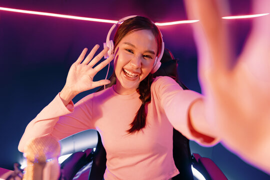 Host channel of young beautiful Asian making selfie photo on smartphone on social media for greeting with fanclub, wearing pastel color headphones, using mic radio at neon colorful studio. Stratagem.