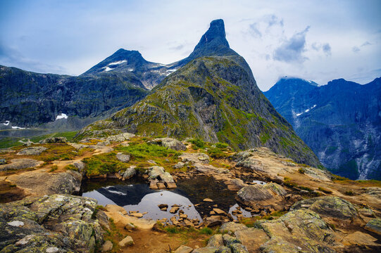 Rugged summit of Litlefjellet in Norway with rocky pools, mossy terrain, sharp alpine peaks, and cloudy sky over the Romsdalen landscape.