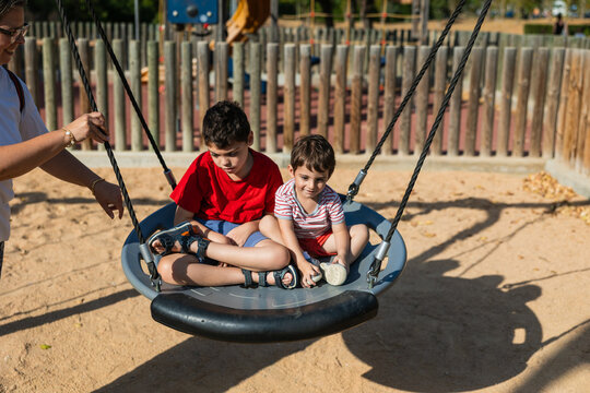 Mother pushing children on accessible swing at playground